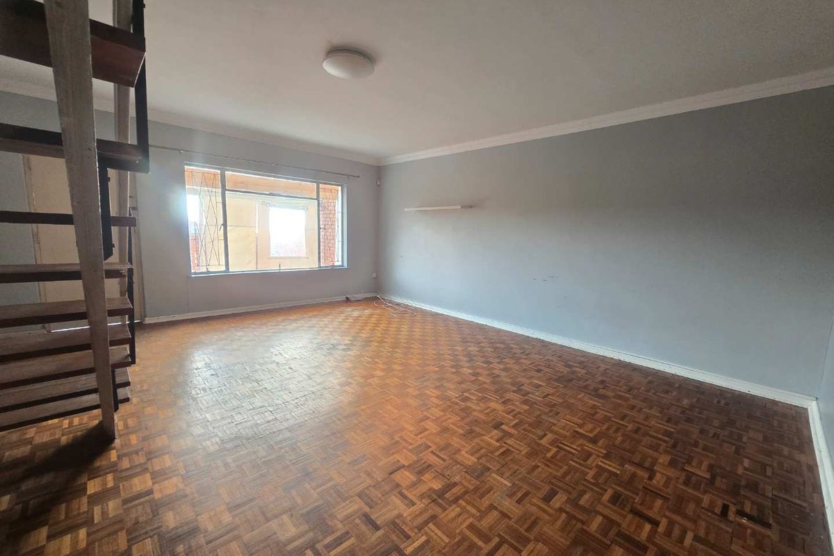 Spacious living area featuring original parquet flooring, a built-in wooden staircase, and large windows providing natural light.