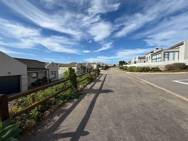 A view of the residential street within the cluster complex, featuring paved roads, neat landscaping, and established boundary fencing.