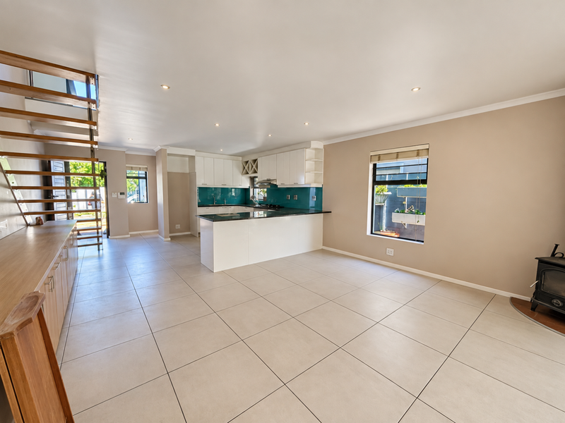 Spacious open-plan living and kitchen area featuring modern white cabinetry, a central island, tiled flooring, a feature staircase, and a cozy wood-burning stove.