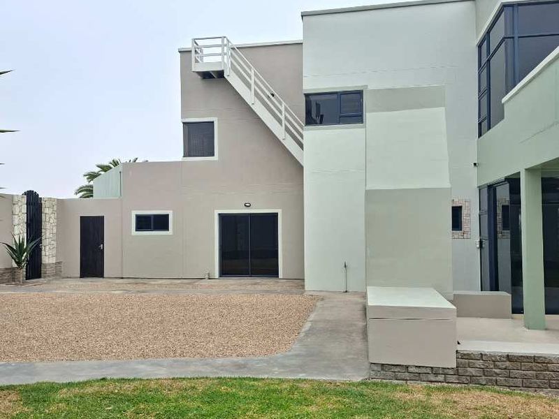 Rear view of a modern multi-level house featuring an external staircase, gravel driveway, and landscaped lawn area.