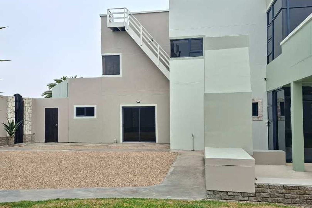 Rear view of a modern multi-level house featuring an external staircase, gravel driveway, and landscaped lawn area.