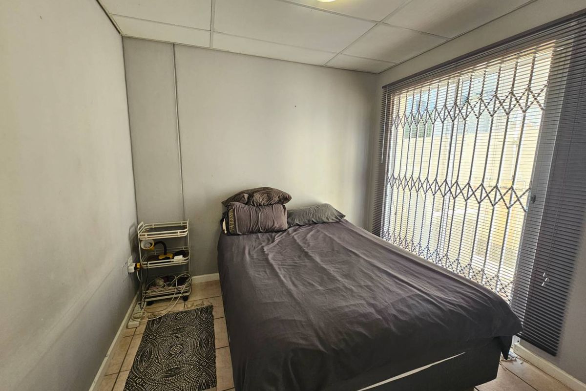 A compact bedroom featuring tiled flooring, a drop ceiling, and a sliding door secured with a metal security gate.