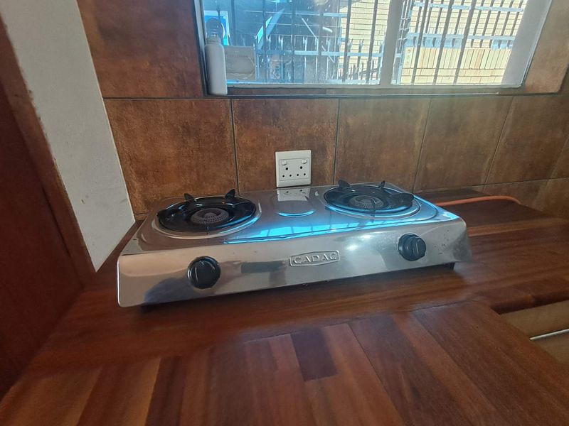 A kitchen area featuring a wooden countertop, tiled backsplash, and a portable gas hob unit.
