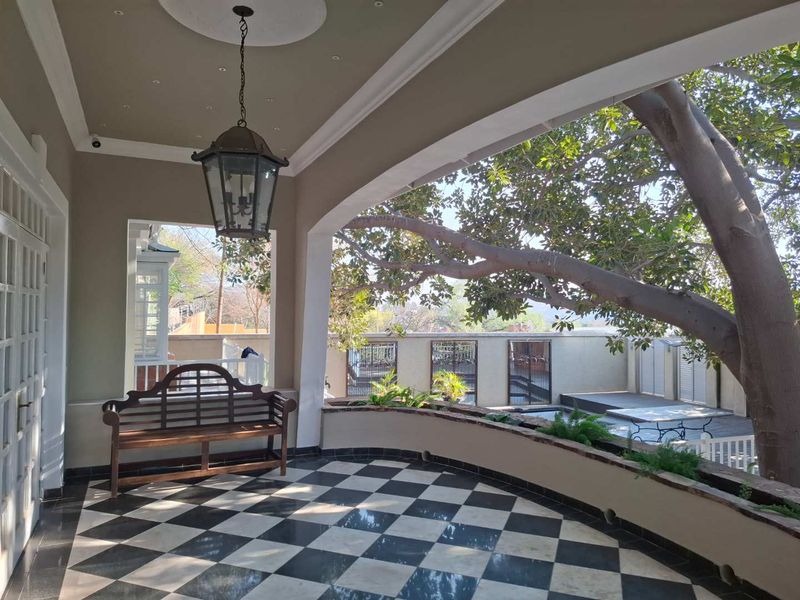 A covered patio featuring elegant checkerboard tiling, a built-in planter box, and decorative ceiling lighting, overlooking the garden area.
