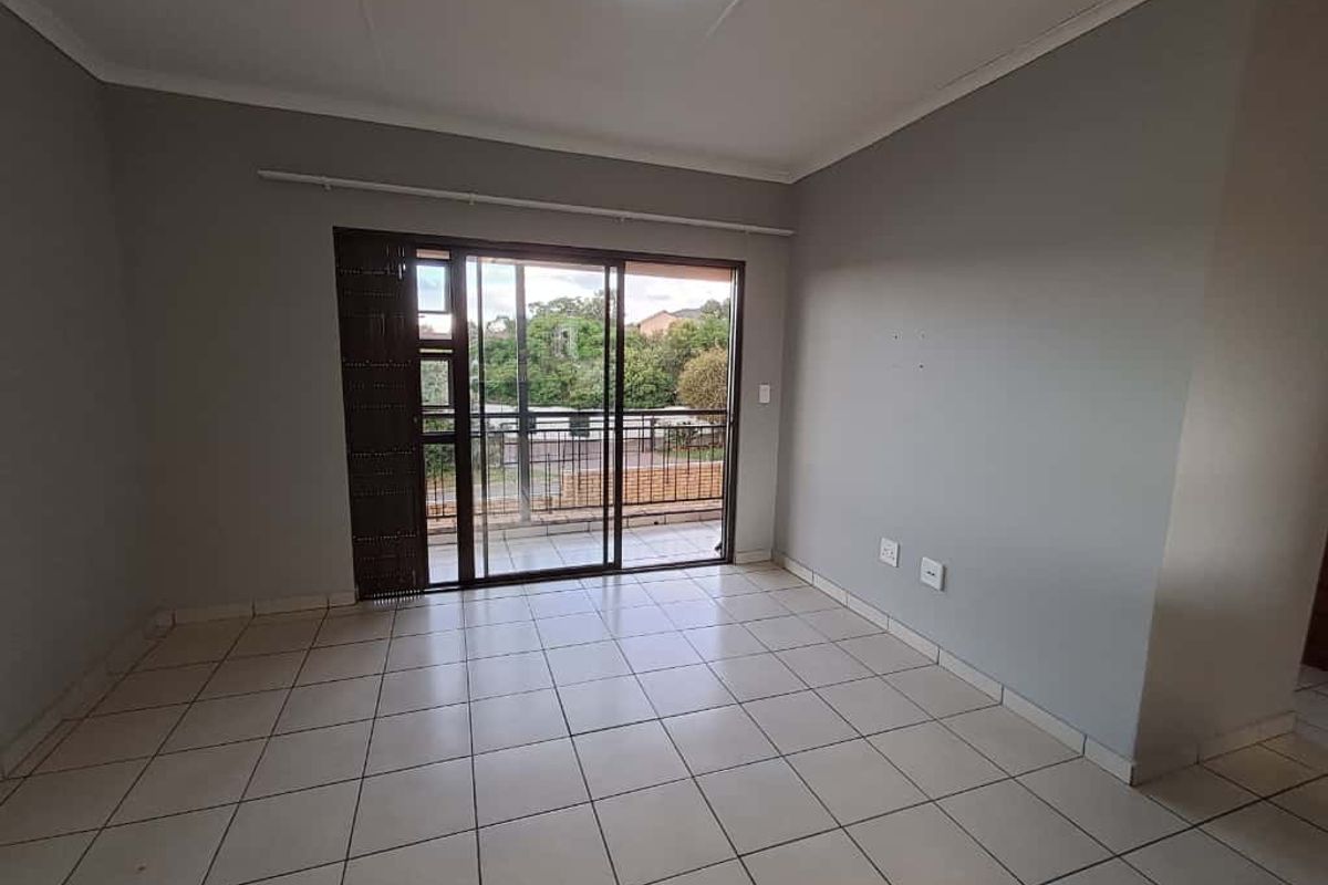 A bright, empty living room featuring neutral tiled flooring, grey walls, and sliding glass doors that open onto a private balcony.