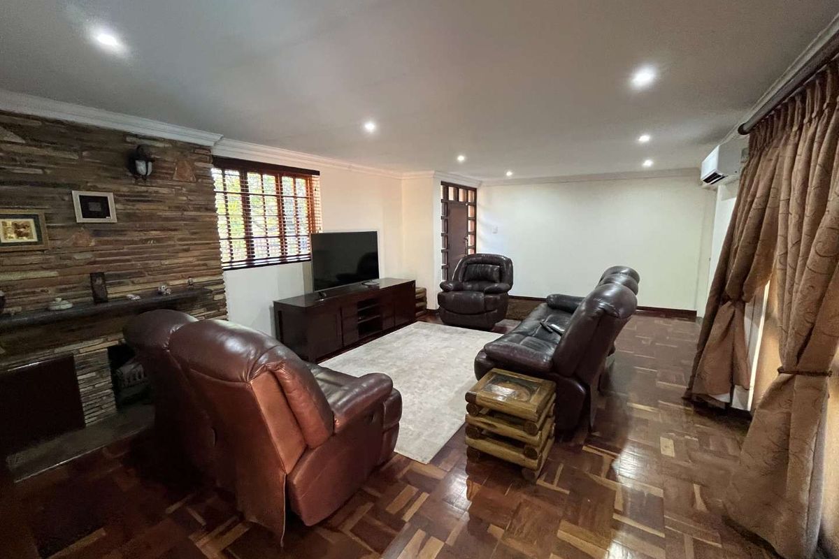 A spacious living room featuring a prominent stone-clad fireplace, polished parquet flooring, recessed downlighting, and a wall-mounted air conditioning unit.