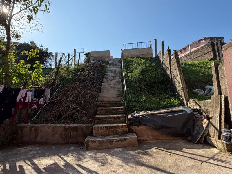 Rear exterior area featuring a concrete staircase leading to an elevated section, with retaining walls and paved ground requiring maintenance and landscaping.