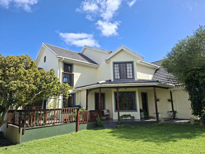 Rear view of a two-story house featuring a covered patio, timber decking, and a well-maintained garden area.