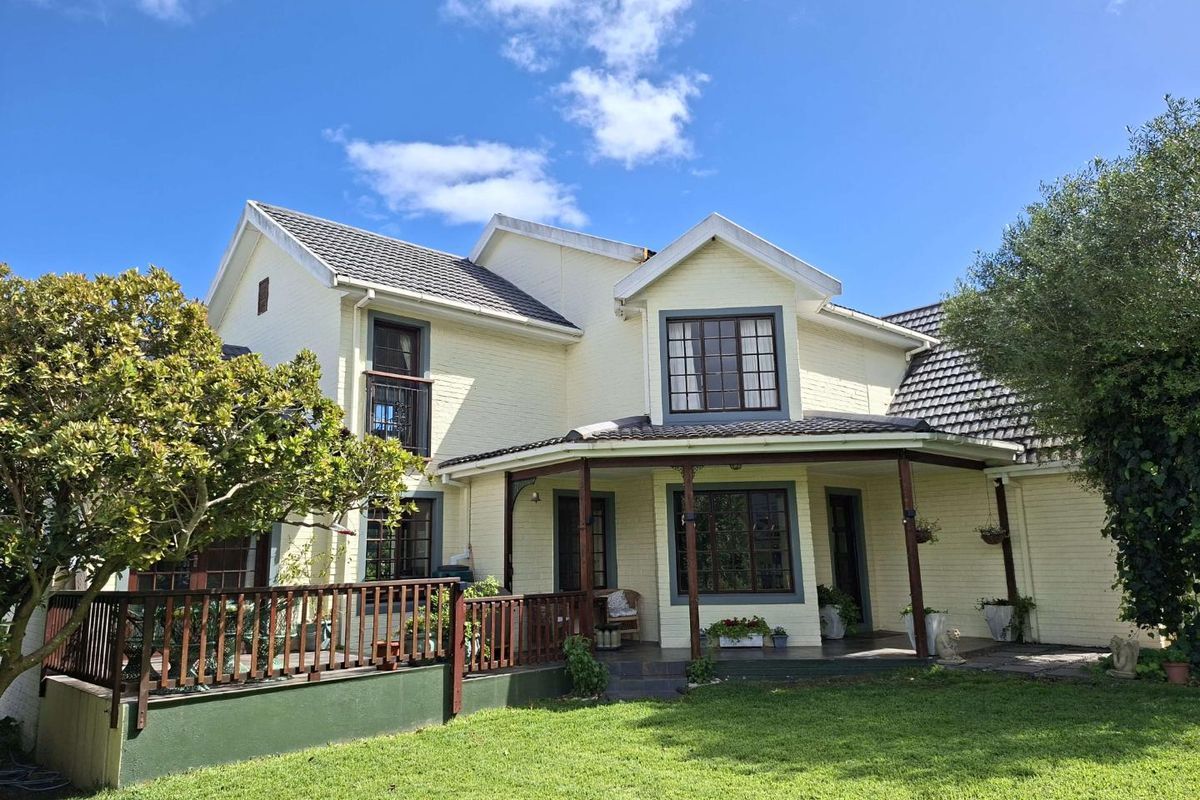 Rear view of a two-story house featuring a covered patio, timber decking, and a well-maintained garden area.
