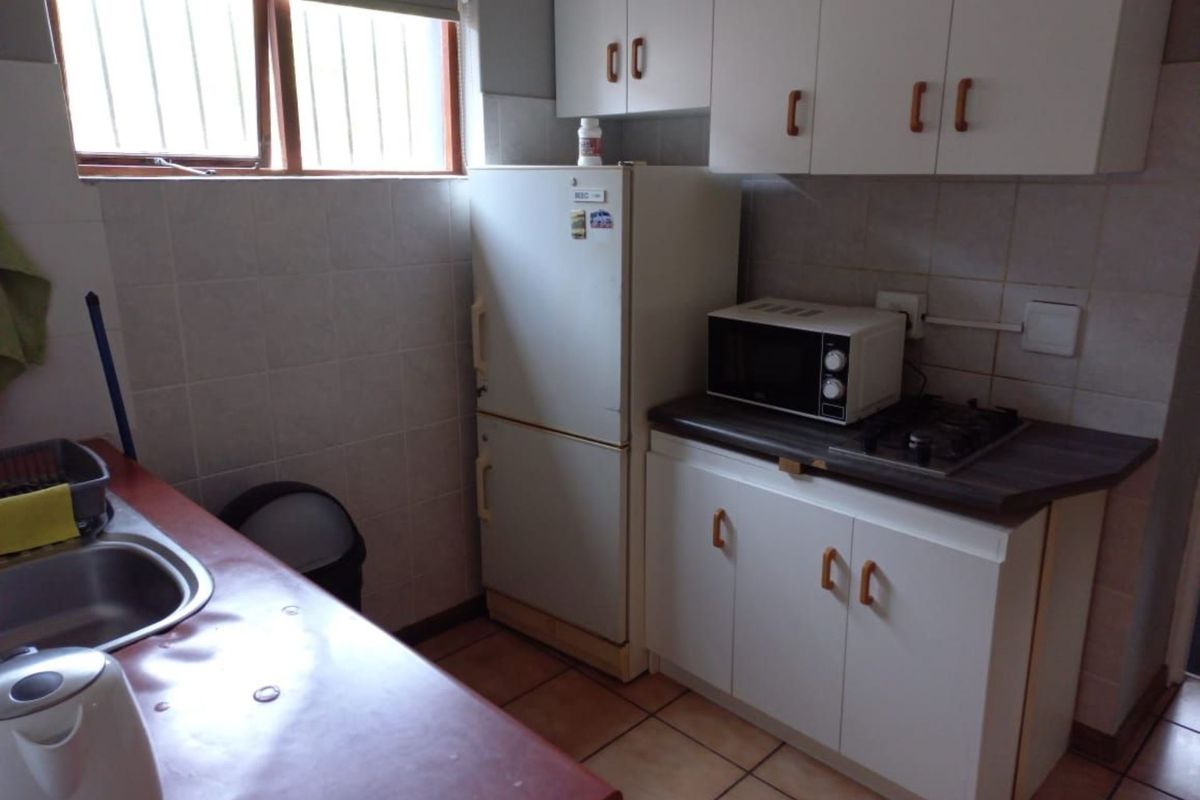 A functional kitchen featuring white cabinetry, tiled splashbacks, a built-in hob, and a stainless steel sink with tiled flooring.