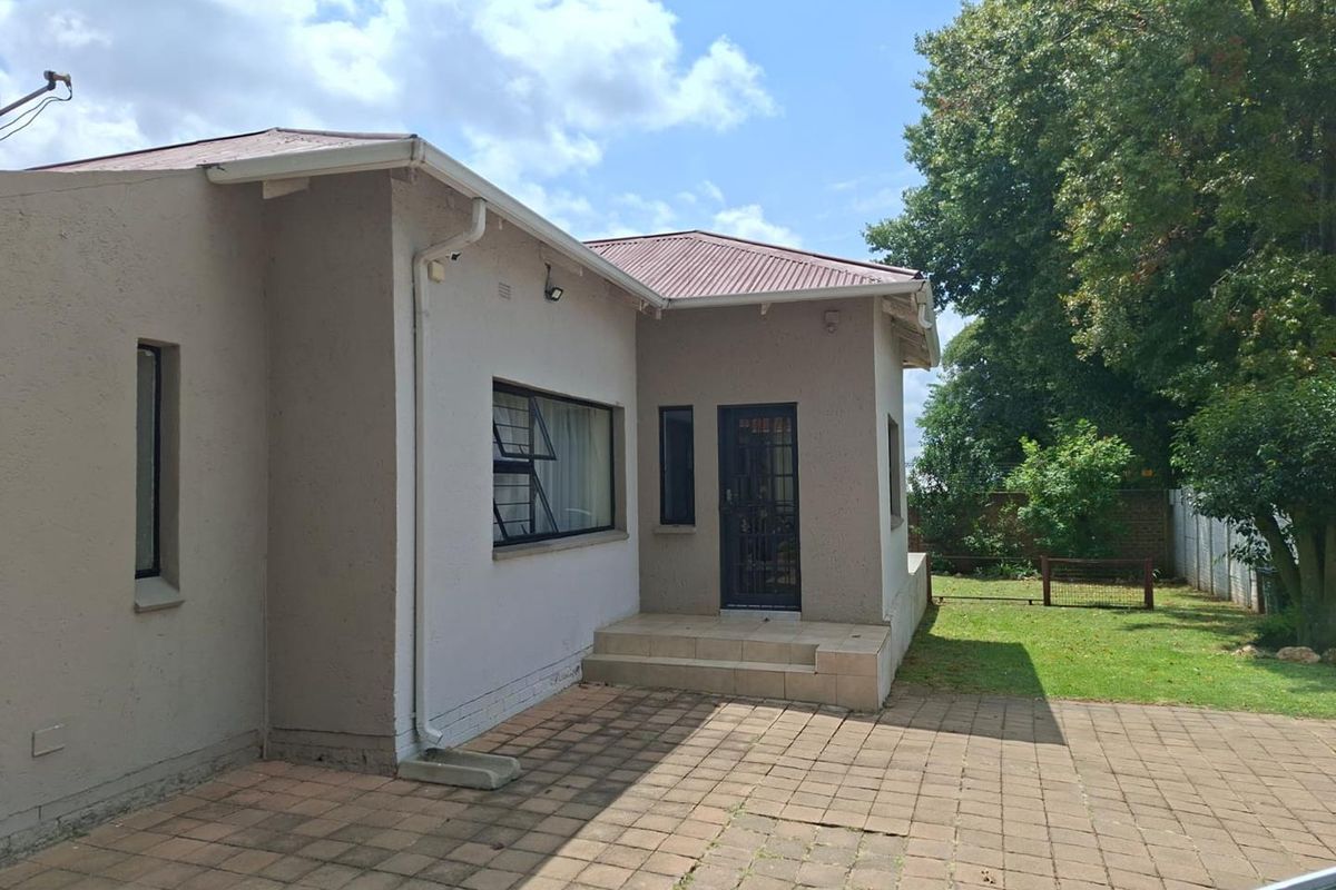 Rear view of the house featuring a paved patio area, metal security door, and access to the garden.