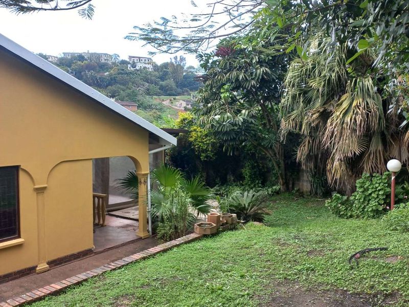Rear view of the property featuring a covered patio area, brick-edged pathways, and a mature garden with established trees and lawn.