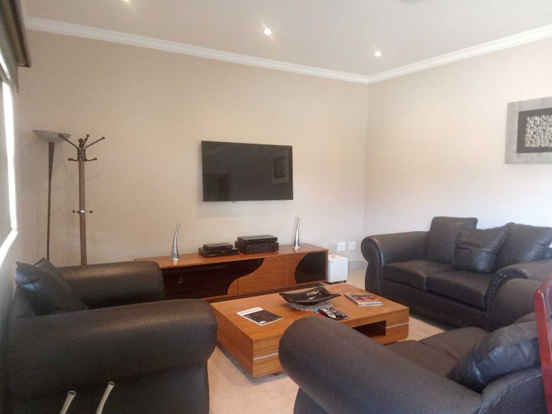 A comfortable living room featuring recessed downlighting, coved ceiling details, and a wall-mounted television setup.