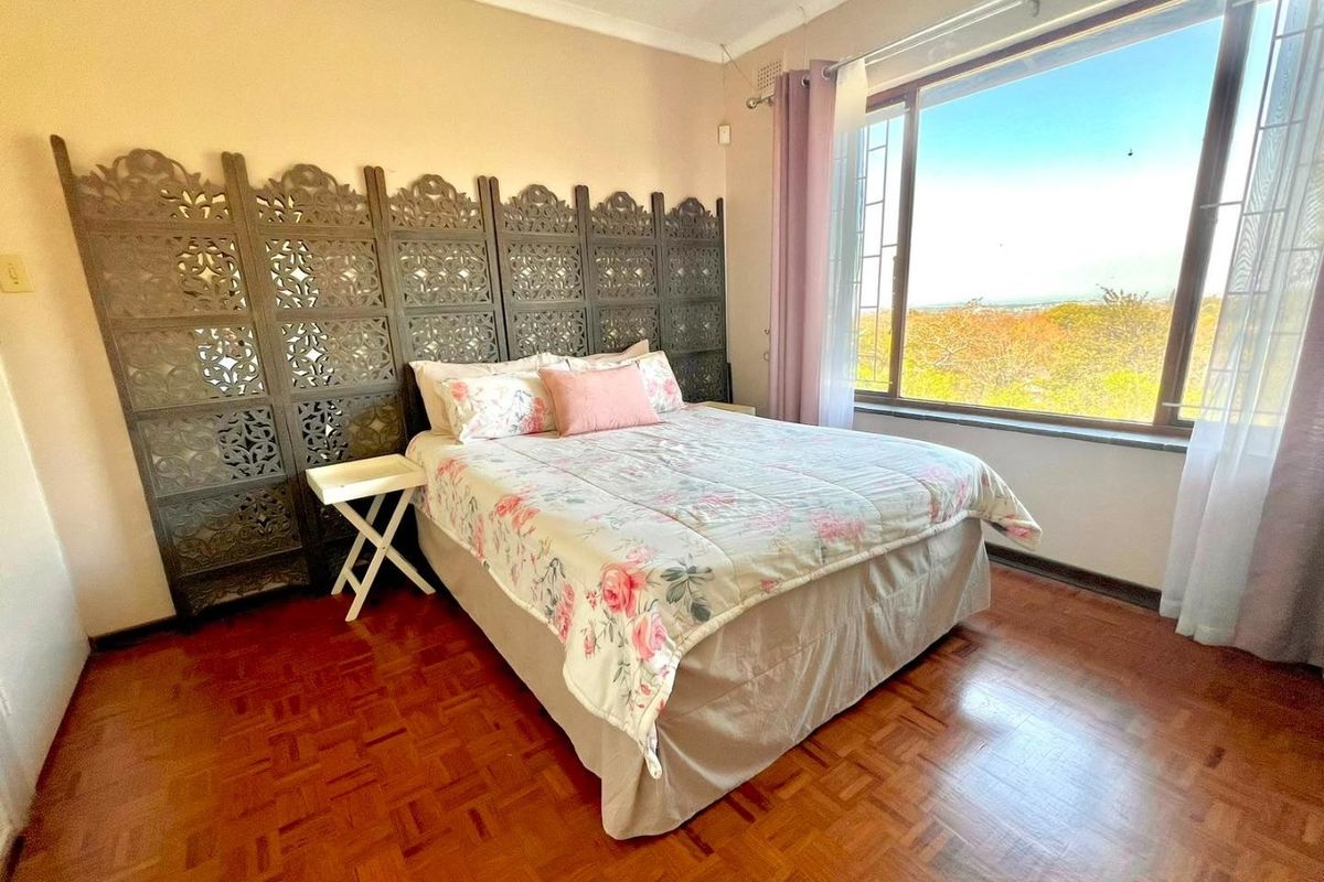 A bedroom featuring parquet flooring, a large window with security bars, and a view of the surrounding landscape.
