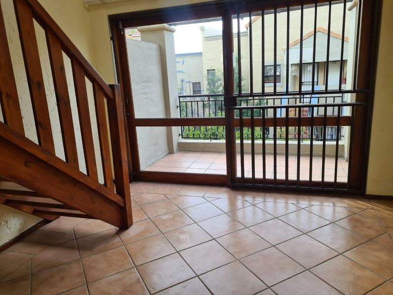 An empty living area featuring tiled flooring, a wooden staircase, and a sliding glass door leading to a private balcony with security gate.