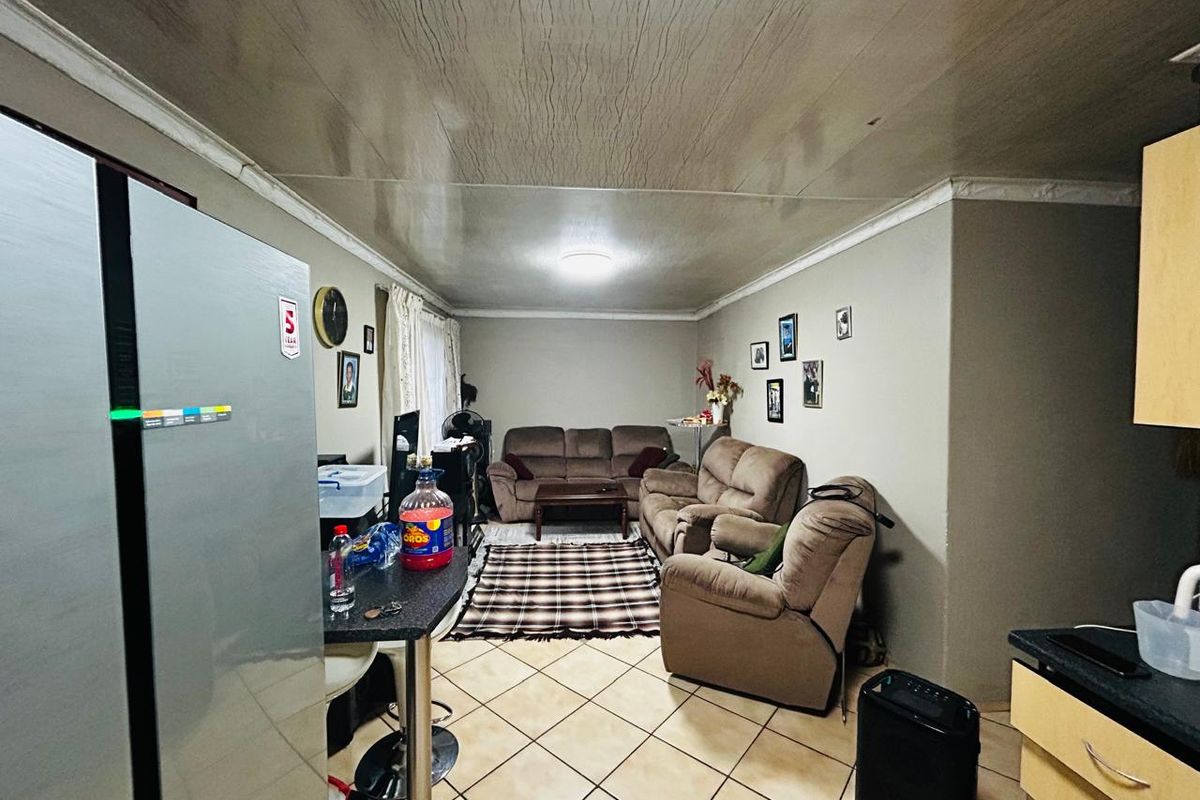 Open-plan living area featuring tiled flooring and integrated kitchen cabinetry, with visible water staining on the ceiling requiring attention.