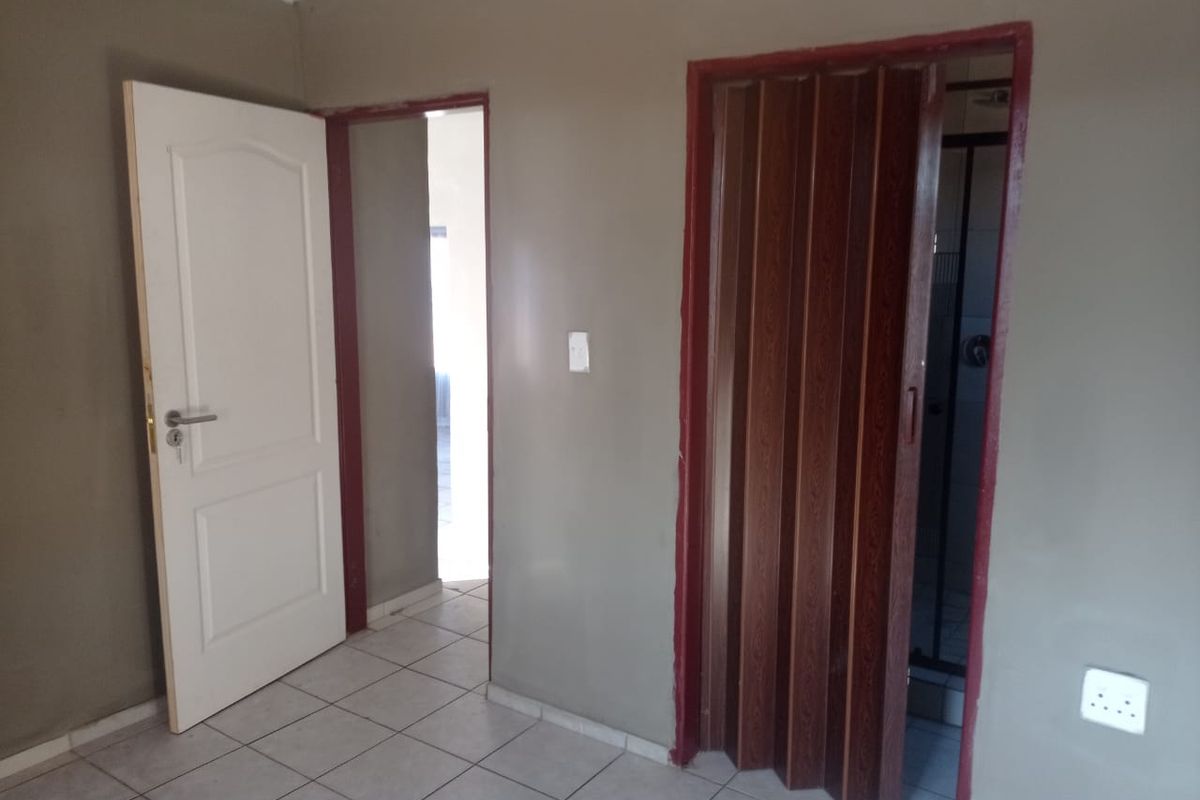 Interior view showing a bedroom with tiled flooring, a white panel door, and a folding wooden door leading to an en-suite bathroom.
