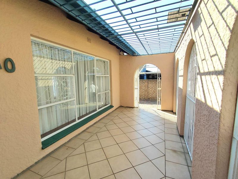 A covered patio area featuring tiled flooring, arched architectural details, and a metal pergola roof, providing a functional outdoor transition space.