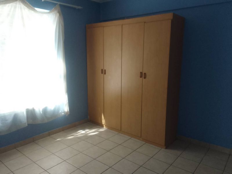 A simple bedroom featuring tiled flooring and a built-in wooden wardrobe, offering a functional space ready for personalization.