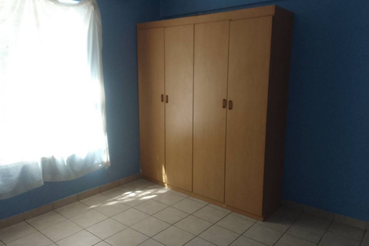 A simple bedroom featuring tiled flooring and a built-in wooden wardrobe, offering a functional space ready for personalization.