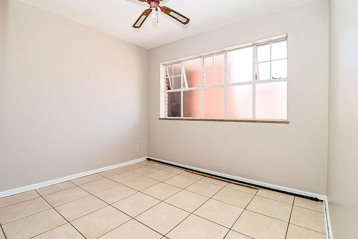 A vacant bedroom featuring neutral wall paint, tiled flooring, and a large window providing natural light.