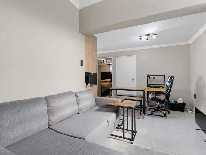 A well-maintained living area featuring neutral wall tones, tiled flooring, and integrated cabinetry, offering a functional and bright open-plan living space.