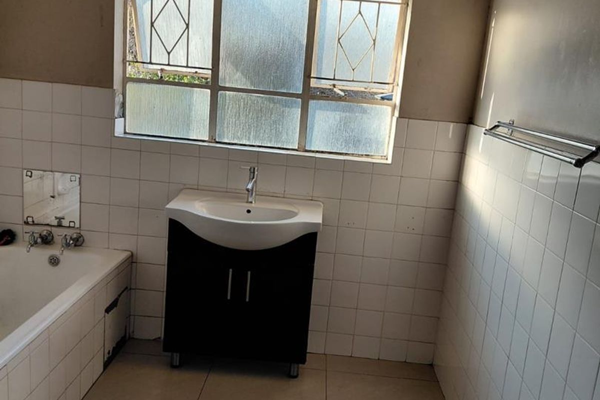 A dated bathroom featuring a built-in bathtub, a modern vanity cabinet with a basin, and tiled walls and flooring.