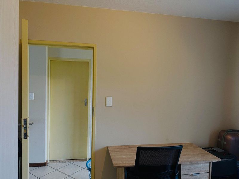 A bedroom interior featuring neutral wall tones, a doorway leading to a tiled hallway, and standard light switches.