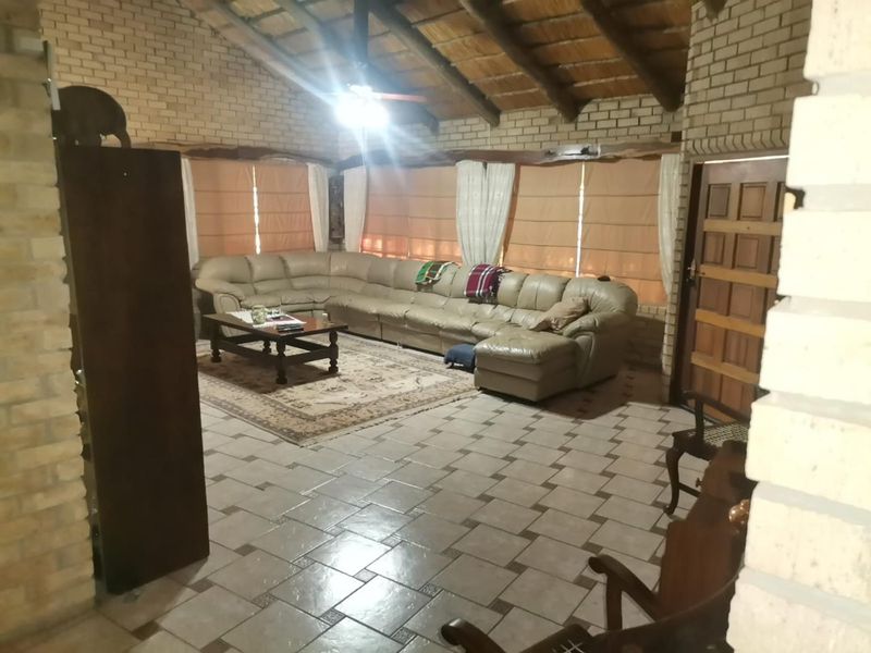 Spacious living room featuring exposed timber beams, face brick walls, and tiled flooring, creating a rustic and comfortable atmosphere.