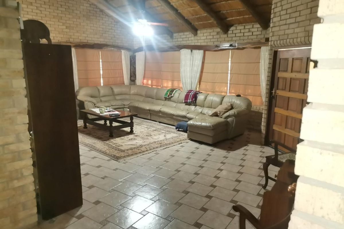 Spacious living room featuring exposed timber beams, face brick walls, and tiled flooring, creating a rustic and comfortable atmosphere.