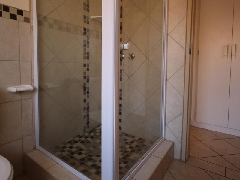 A functional bathroom featuring a tiled shower enclosure, ceramic floor and wall tiling, and a built-in storage cupboard.