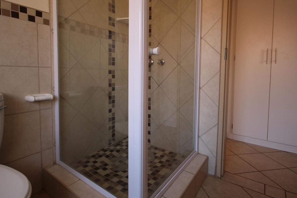 A functional bathroom featuring a tiled shower enclosure, ceramic floor and wall tiling, and a built-in storage cupboard.