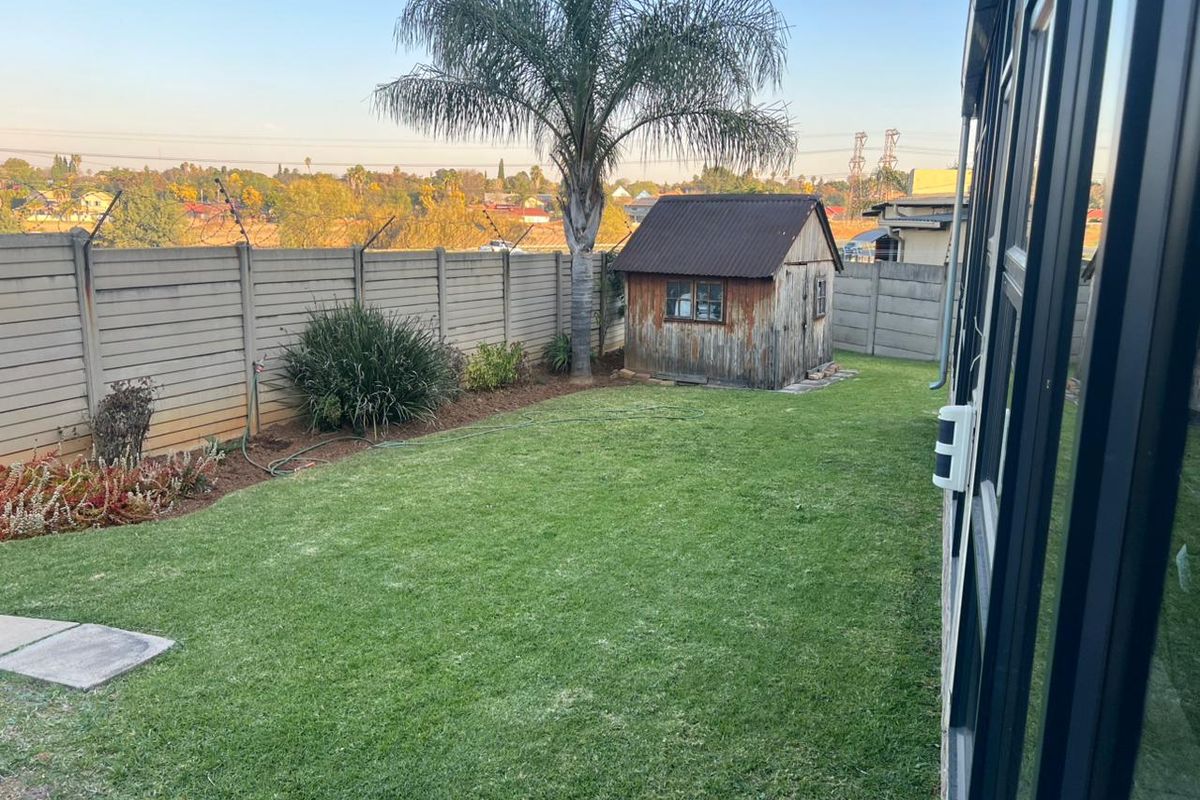 A rear garden featuring a lawn, perimeter precast concrete walling, and a weathered timber garden shed.