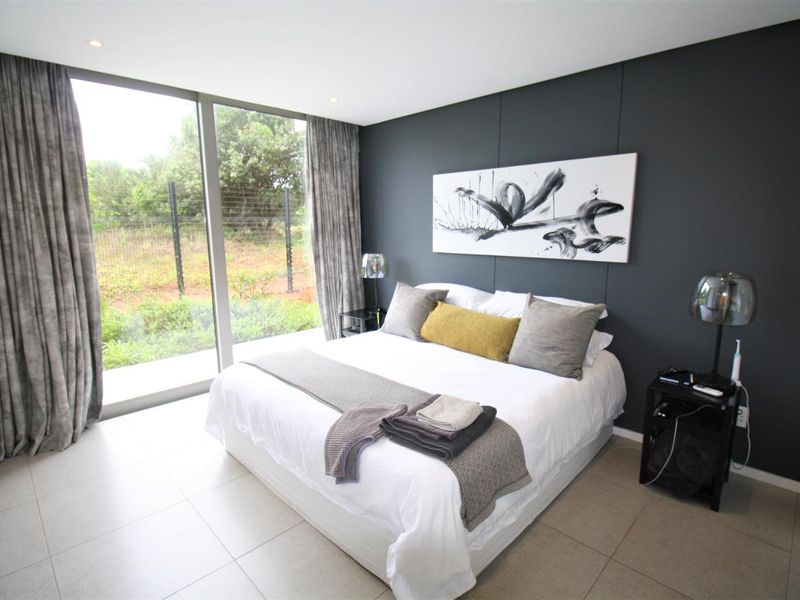 Modern bedroom featuring large floor-to-ceiling windows, neutral tiled flooring, and a dark feature wall, offering a bright and contemporary living space.