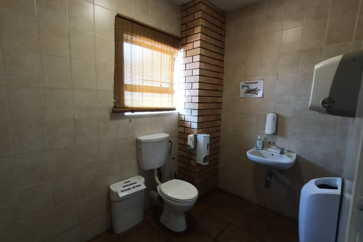 A functional industrial-style bathroom featuring tiled walls, a wall-mounted basin, and an exposed brick feature pillar.