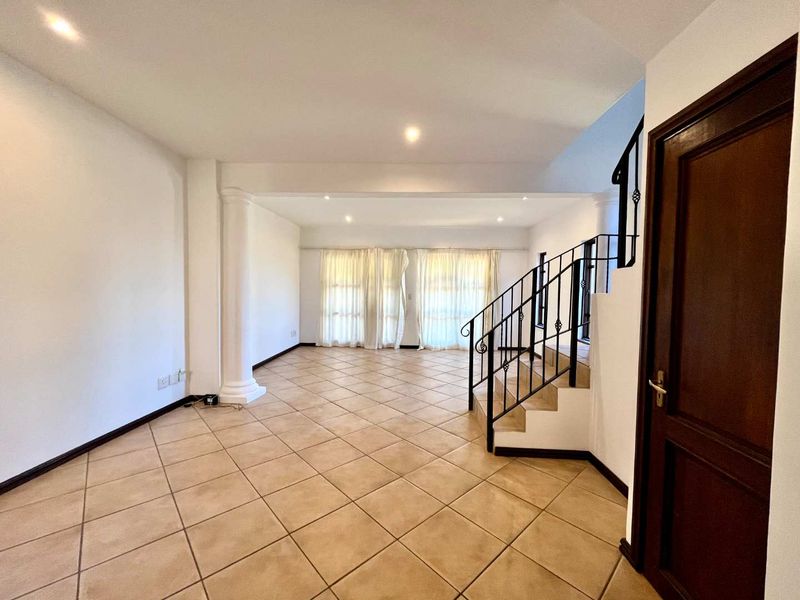 Spacious, open-plan living area featuring neutral tiled flooring, a decorative column, and a wrought iron staircase leading to the upper level.