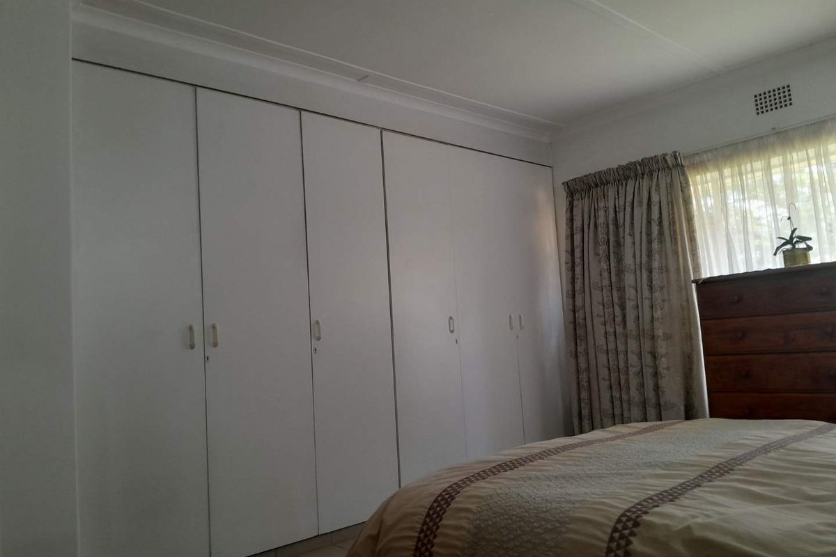 A bedroom featuring a large wall-to-wall built-in wardrobe with white cabinetry and a window with curtain treatments.