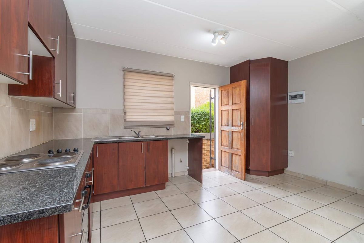 Functional kitchen featuring dark wood cabinetry, granite countertops, integrated hob, tiled flooring, and direct access to the exterior.