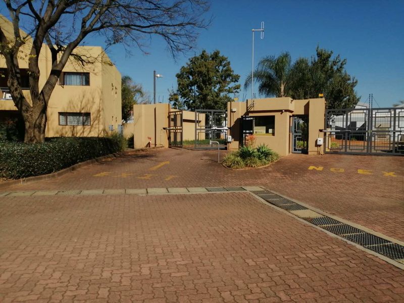 View of the apartment complex entrance featuring a paved driveway, security gate, and guard house with electric fencing.