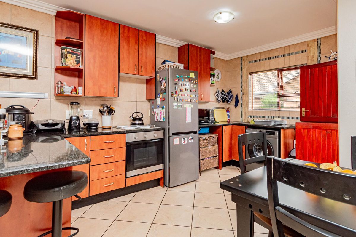 A functional kitchen featuring wood-toned cabinetry, granite countertops, a built-in oven and hob, and tiled flooring with an integrated dining area.