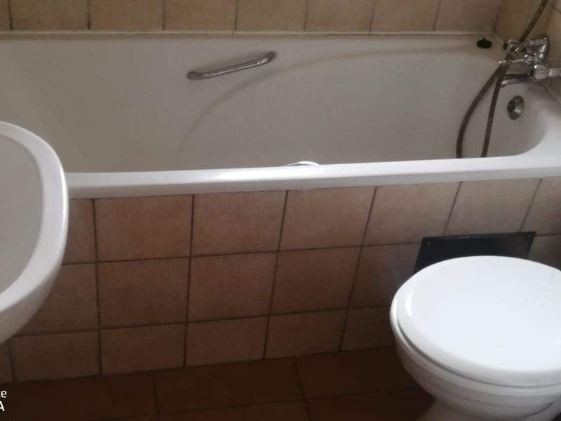 A functional bathroom featuring a standard bathtub, pedestal basin, and toilet with neutral wall and floor tiling.