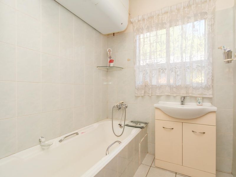 A functional bathroom featuring a bathtub, vanity cabinet with washbasin, and wall-mounted water heater, finished with neutral wall and floor tiles.