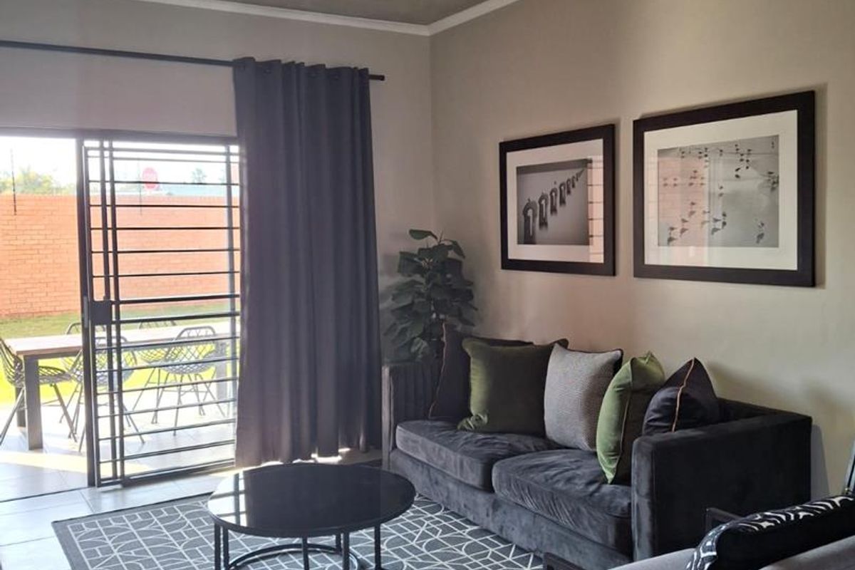 A modern living room featuring tiled floors, track lighting, and a sliding glass door providing direct access to the outdoor patio area.