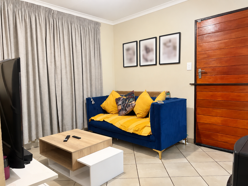 A living room featuring tiled flooring and a solid wooden entrance door, finished with neutral wall paint and curtain tracks.