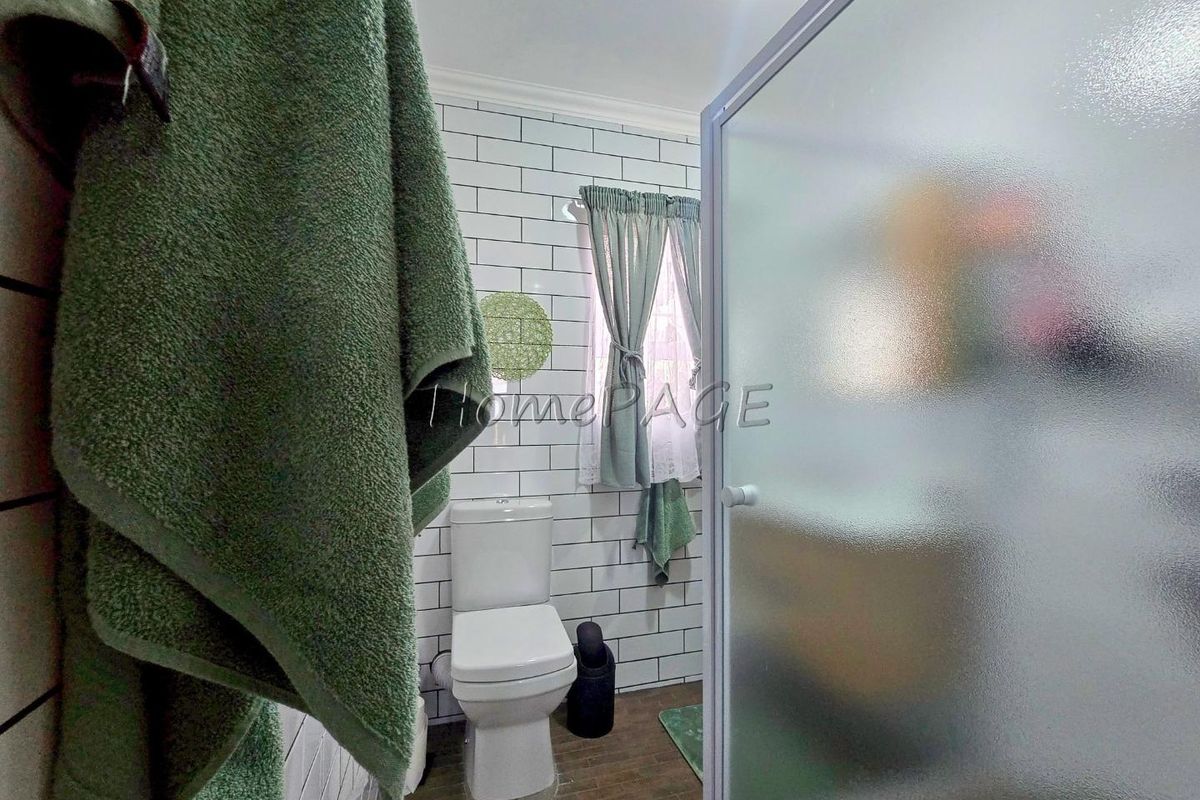 A functional bathroom featuring subway-style wall tiling, a standard toilet, and a glass-enclosed shower unit.