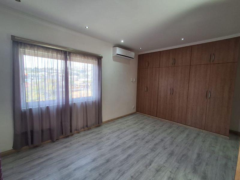 A spacious bedroom featuring modern laminate flooring, extensive built-in wooden cupboards, and a wall-mounted air conditioning unit.