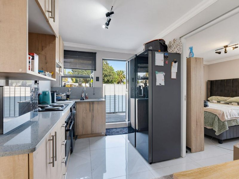 A functional kitchen featuring light wood cabinetry, stone countertops, integrated appliances, and tiled flooring, with direct access to an outdoor area.