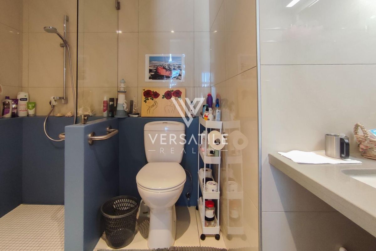 A functional bathroom featuring a walk-in shower with glass screen, wall-mounted grab rail, toilet, and a built-in vanity countertop.