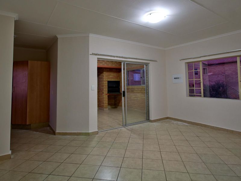 Spacious living area featuring tiled flooring, a sliding door leading to a built-in brick braai area, and neutral wall finishes.