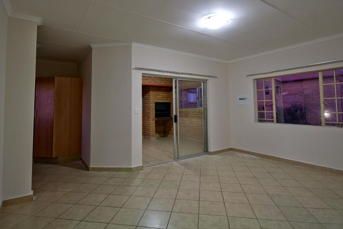 Spacious living area featuring tiled flooring, a sliding door leading to a built-in brick braai area, and neutral wall finishes.